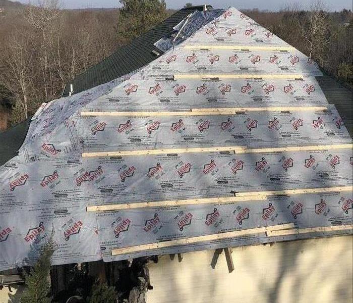 A large roof protected with a tarp after experiencing wind damage