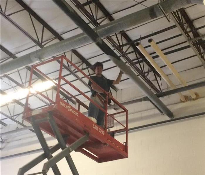 A SERVPRO employee in a sicissor lift cleaning dust from a rafter at a Scranton plastic manufacturer.