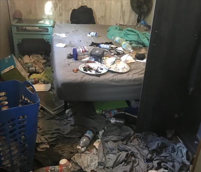 A bedroom in disarray from neglect. Clothes and food thrown on the ground
