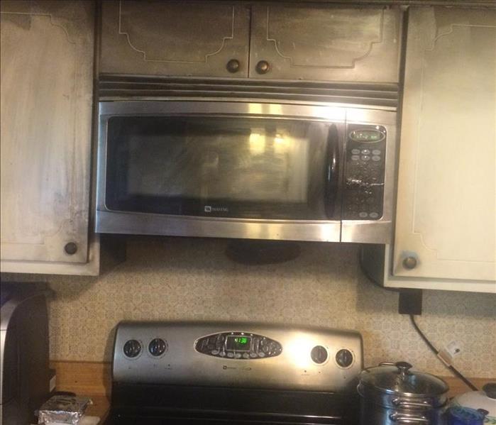 A picture of a stove and microwave damaged by a grease fire. They are soot covered.