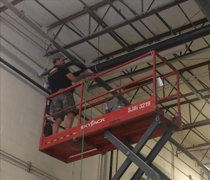 A SERVPRO employee in a scissor lift cleaning a high ceiling at a local manufacturing facility 